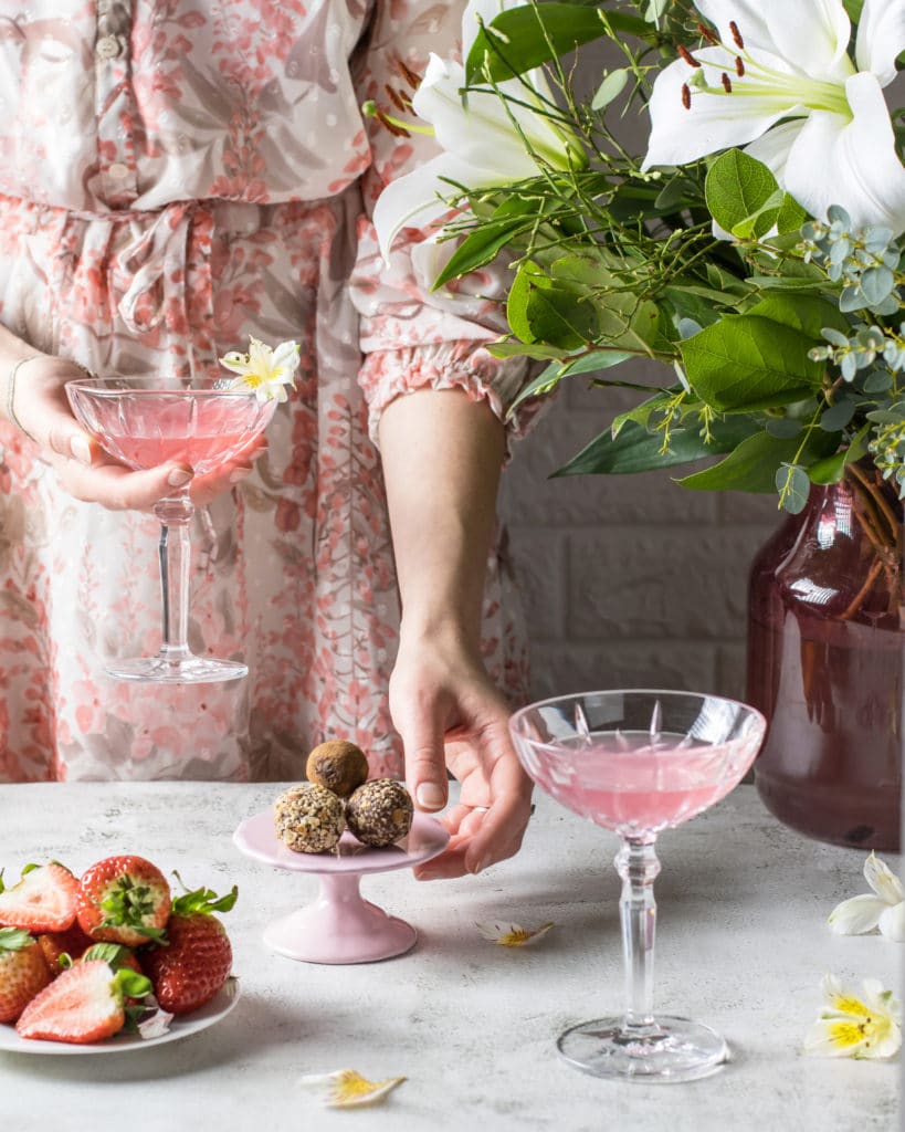 Pink coctail with flowers, strawberries and chocolate balls
