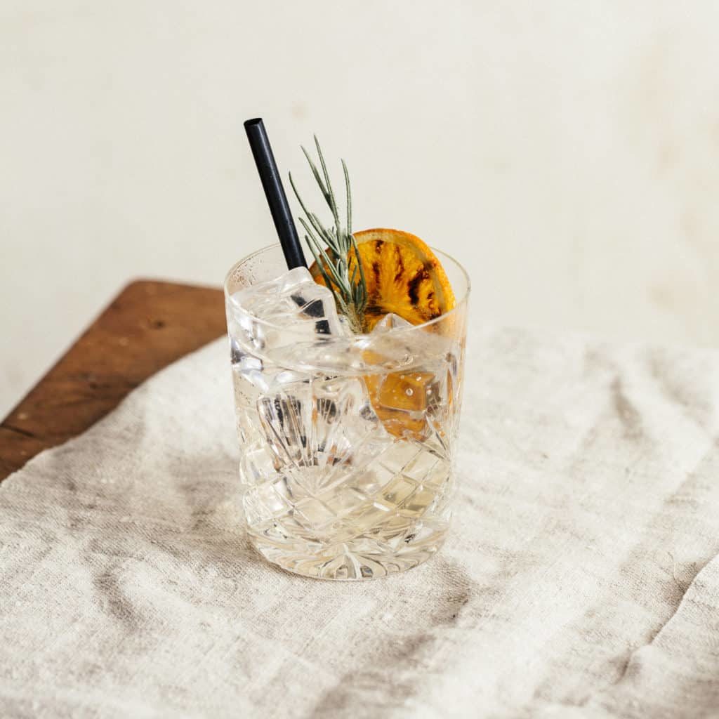 Gin tonic garnished with charred orange and lavender, on a rustic table